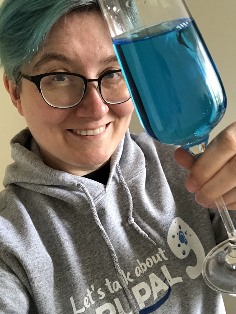 Webchick with blue hair holding a glass with blue pop towards camera.