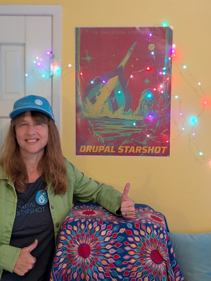 Kristen Pol, a long time Drupal community member, showing off Drupal Starshot swag (tshirt, hat, and poster) in bright colors of teal, red, yellow and more