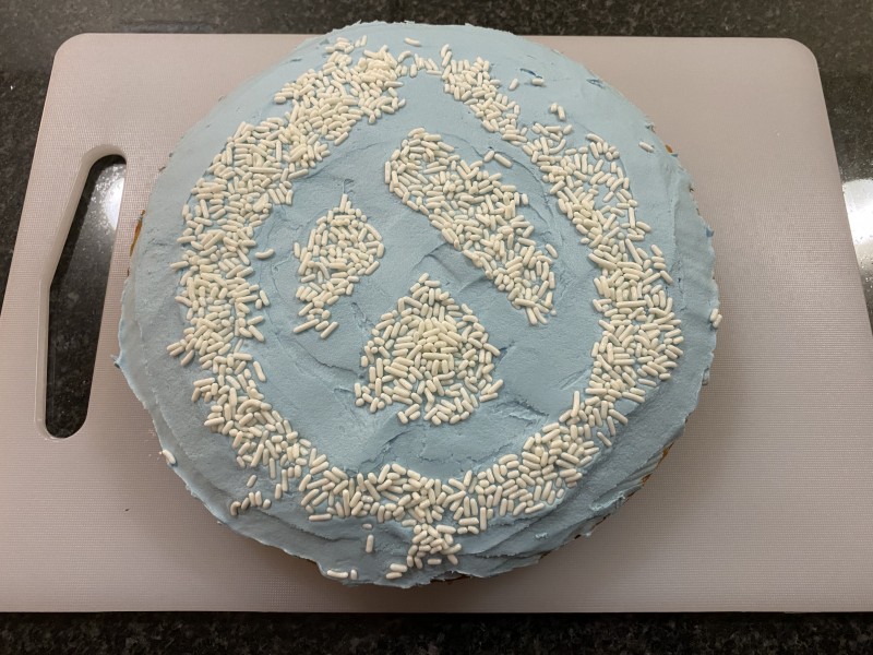 Homemade blue round cake with the Drupal drop evergreen logo in white sprinkles