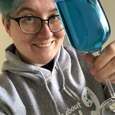 Webchick with blue hair holding a glass with blue pop towards camera.